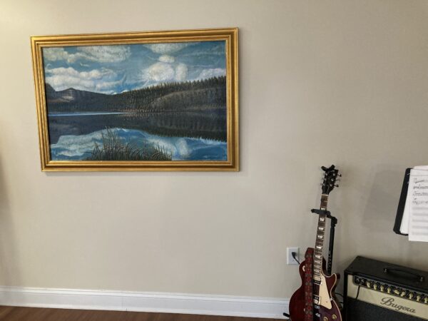 A guitar sitting in front of a painting on the wall.