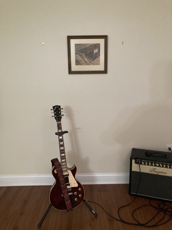 A guitar sitting in front of a picture on the wall.