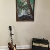 A guitar and an amp in front of a painting.