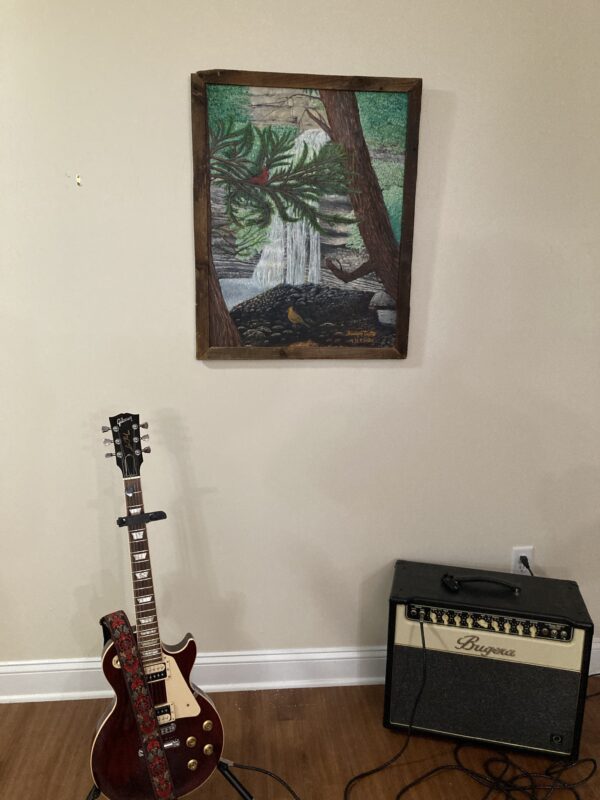 A guitar and an amp in front of a painting.