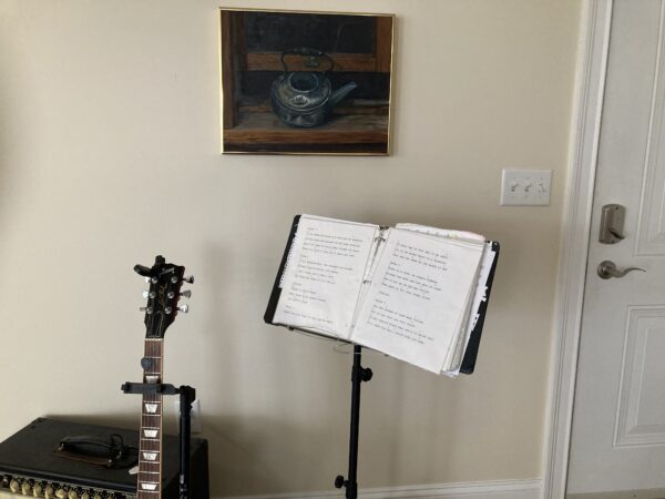 A guitar and a book stand in front of a painting.