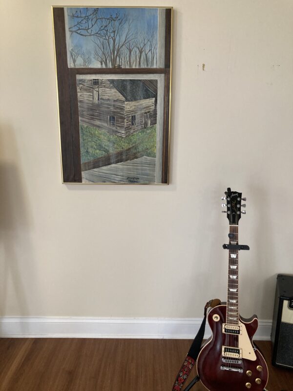 A guitar sitting in front of a painting.