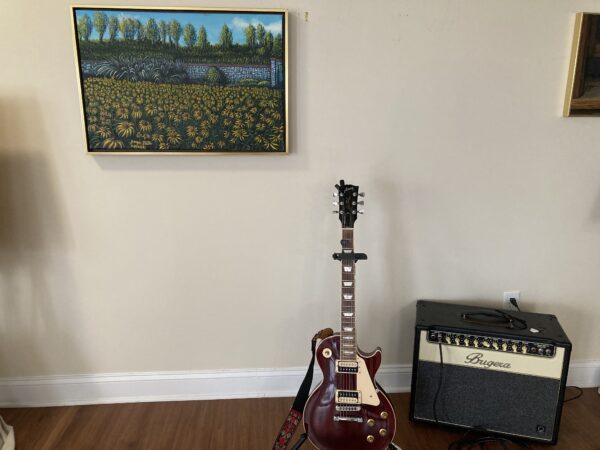 A guitar sitting in front of a painting.