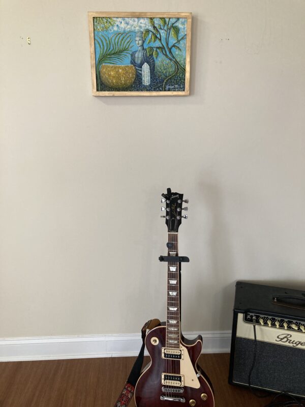 A guitar sitting in front of a picture on the wall.